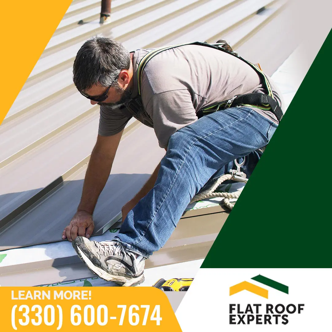A roofer wearing a safety harness installing standing seam metal roofing panels, featured with Flat Roof Experts logo and contact number.